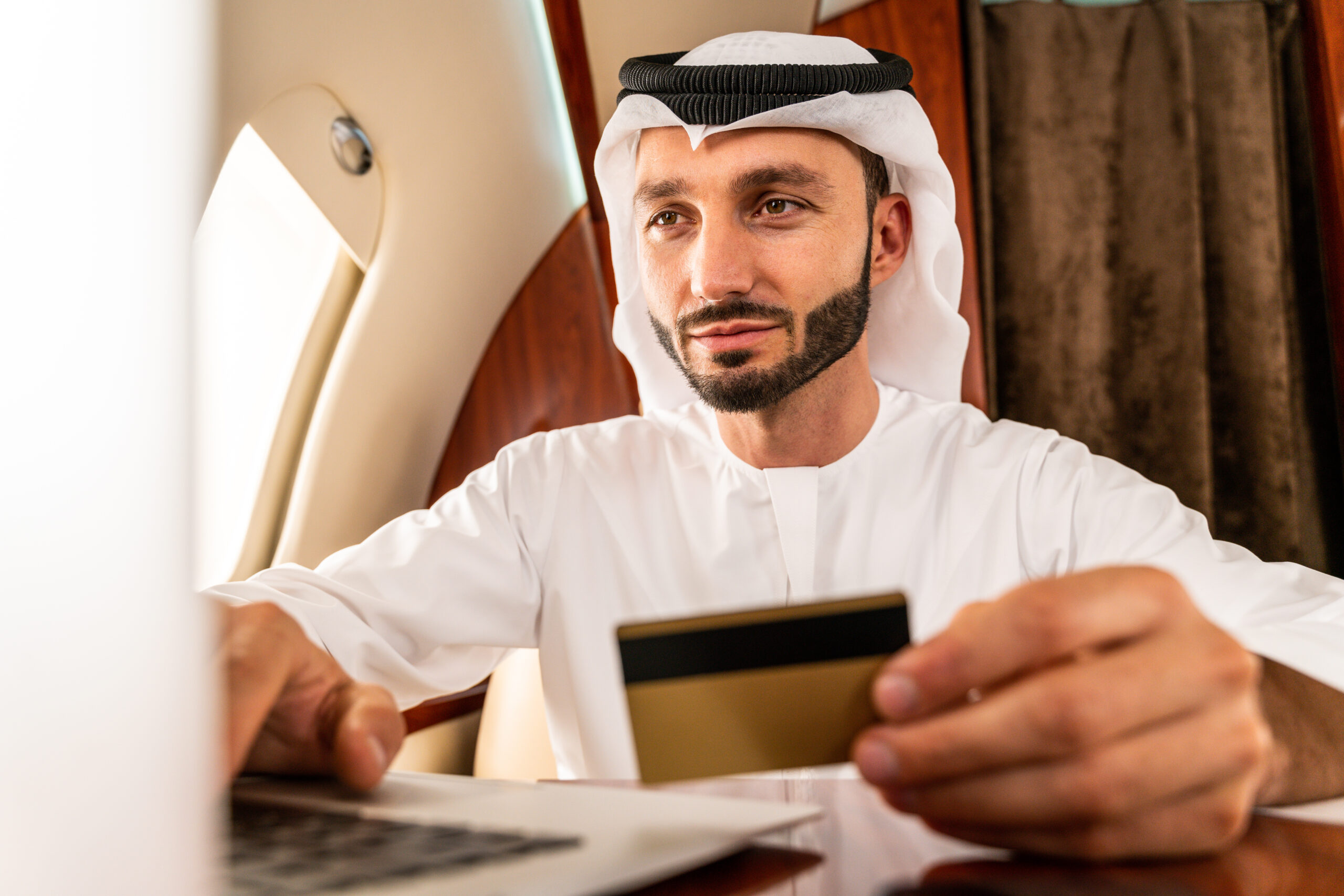 Arabic man wearing kandora in emirates style flying on exclusive private jet - Middle-eastern businessman with traditional dress flies in exclusive business class on airplane, concepts about business and trasportation