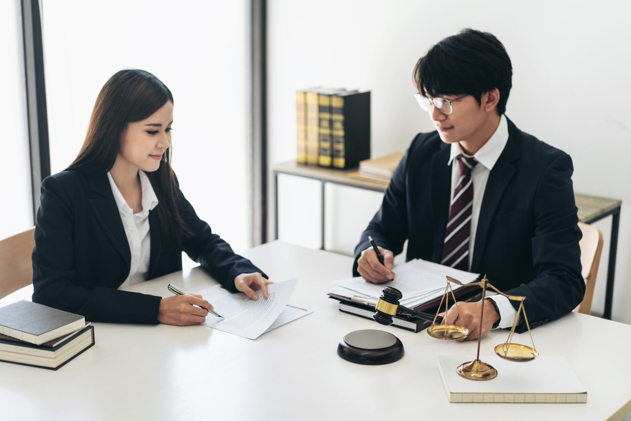 Male lawyer holding justice hammer and reading business document while giving advice about litigation case and legal contract with businesswoman in law firm office.