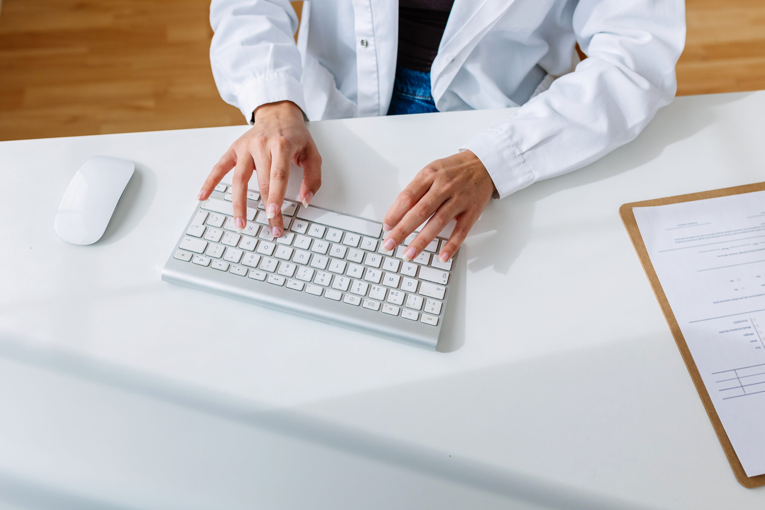 Unrecognizable female doctor working on laptop at clinic office. Top view of practitioner hands typing on keyboard sitting at hospital desk.